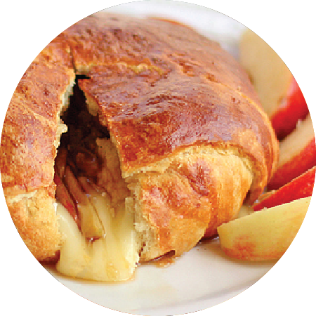 Closeup of apple brie crescent wrap bake sliced open with cheese melting out onto plate and a side of fresh apples