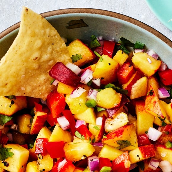 Closeup of peach salsa in a bowl served with a tortilla chip